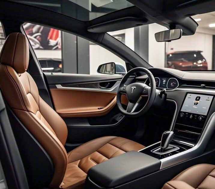 2025 Tesla Model Y Juniper interior with luxurious brown leather seats, panoramic glass roof, and advanced touchscreen dashboard in a modern showroom.